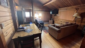 Interior acogedor de una cabaña de madera con una mesa de comedor, sillas, un sofá y un televisor.
