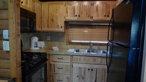 A kitchen with wooden cabinets, a stove, a refrigerator, a sink, and a window with blinds.