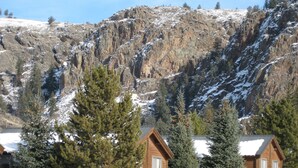 A cabin with a wooden exterior, surrounded by snow-covered ground and trees, with a mountainous backdrop.