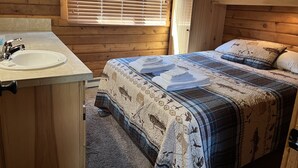 A wooden cabin room with a bed, a sink, and a window with blinds.