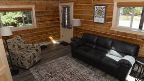 A log cabin interior with a black leather sofa, patterned armchair, and a rug. - Roomy Taylor Canyon Cabin With Private Fishing Access (Almont)