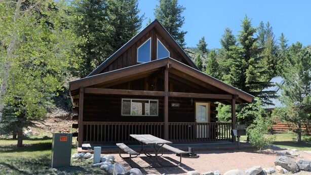 A wooden cabin with a picnic table and benches in front, surrounded by rocks and trees. - Roomy Taylor Canyon Cabin With Private Fishing Access (Almont)
