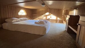 A cozy attic bedroom with a large bed, wooden walls, and a small window. - Modern "Tiny Home" Style Cabin on Taylor River with Private Fishing Access (Almont)