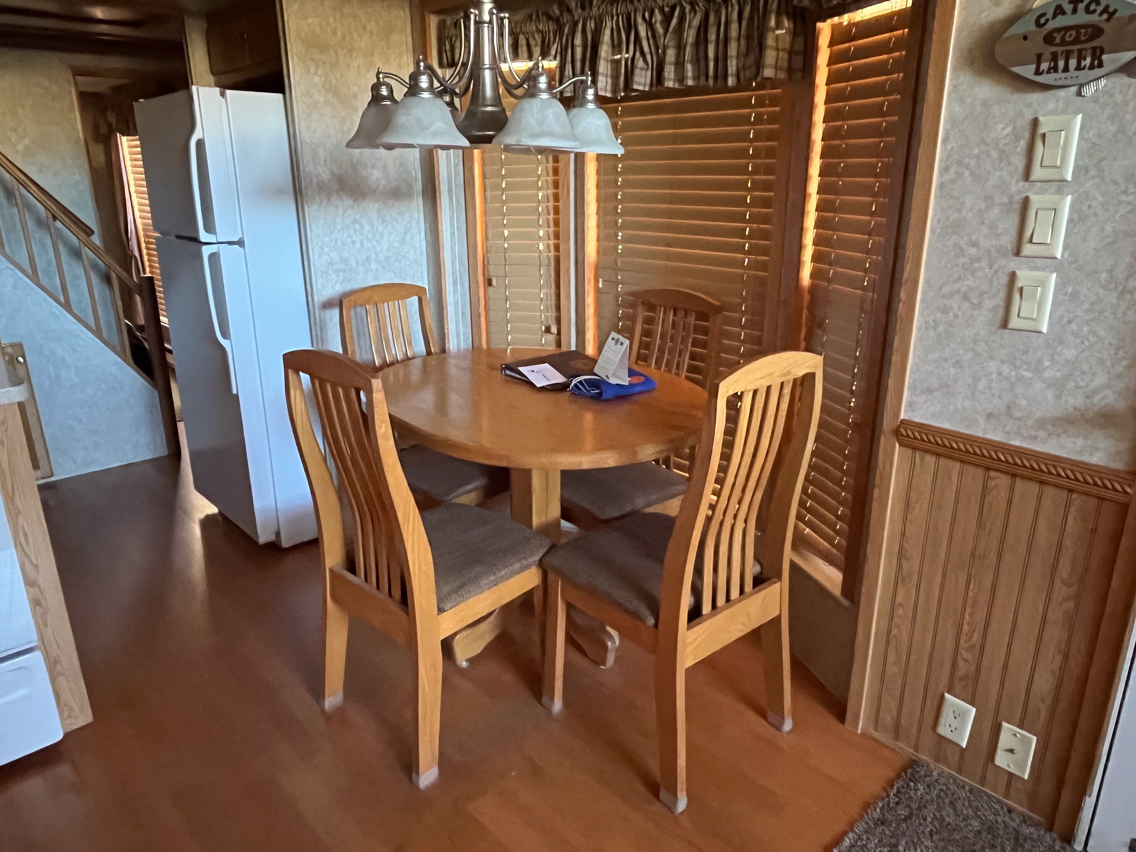 Zona pranzo con tavolo e sedie in legno, frigorifero e lampada a parete.