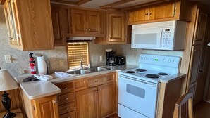 A compact kitchen with wooden cabinets, a white stove, a microwave, and a sink. - Modern "Tiny Home" Style Cabin on Taylor River with Private Fishing Access (Almont)