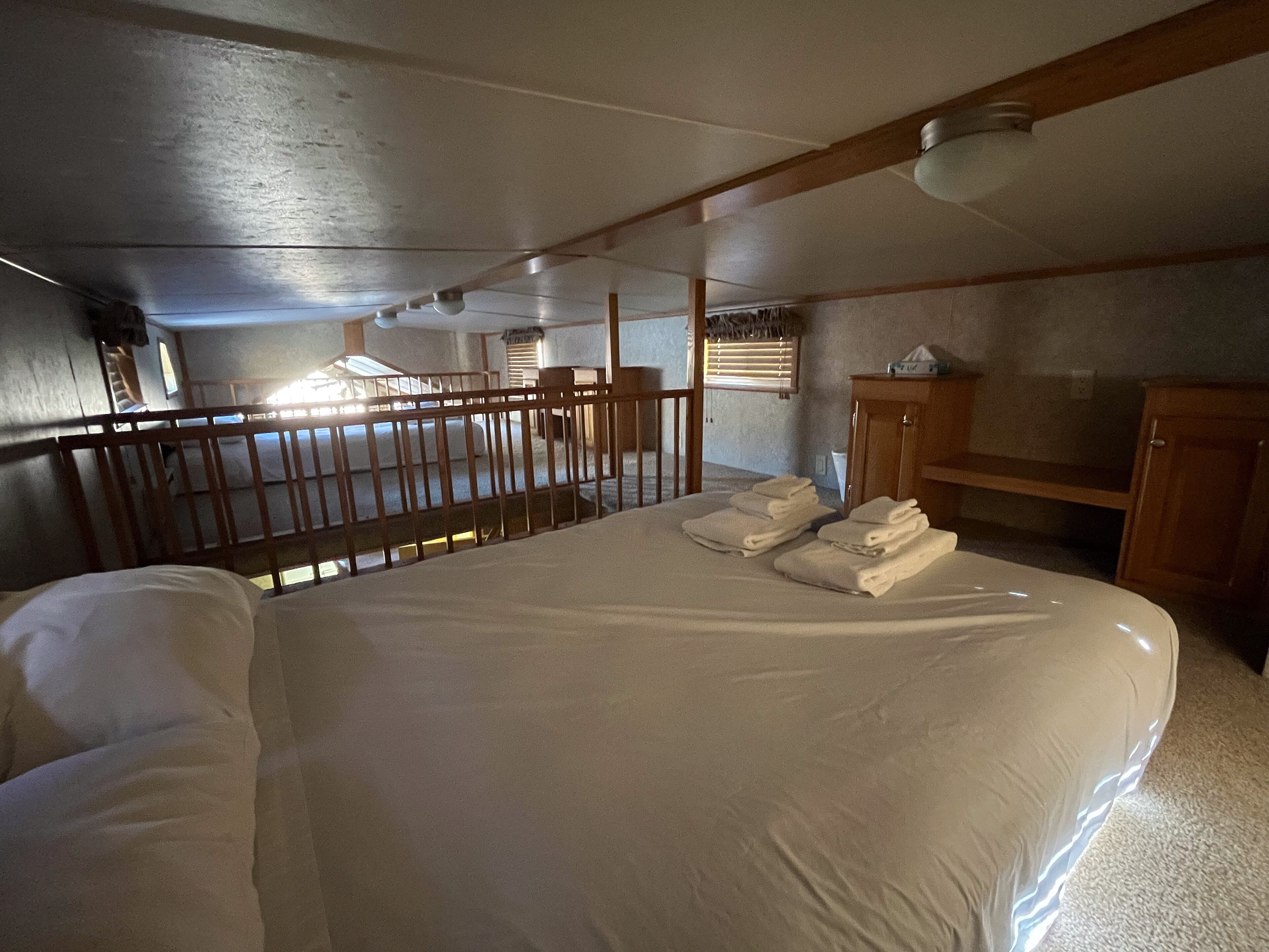 A hotel room with a large bed, wooden headboard, a small desk, and a window with blinds.