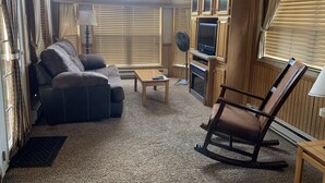 A cozy living room with a leather sofa, a rocking chair, a coffee table, and a TV on a wooden stand.