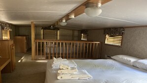 A bedroom with a large bed, a wooden crib, a desk, and a window with blinds.