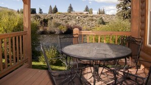 A covered outdoor patio with a round table and chairs, overlooking a river and a mountainous landscape.