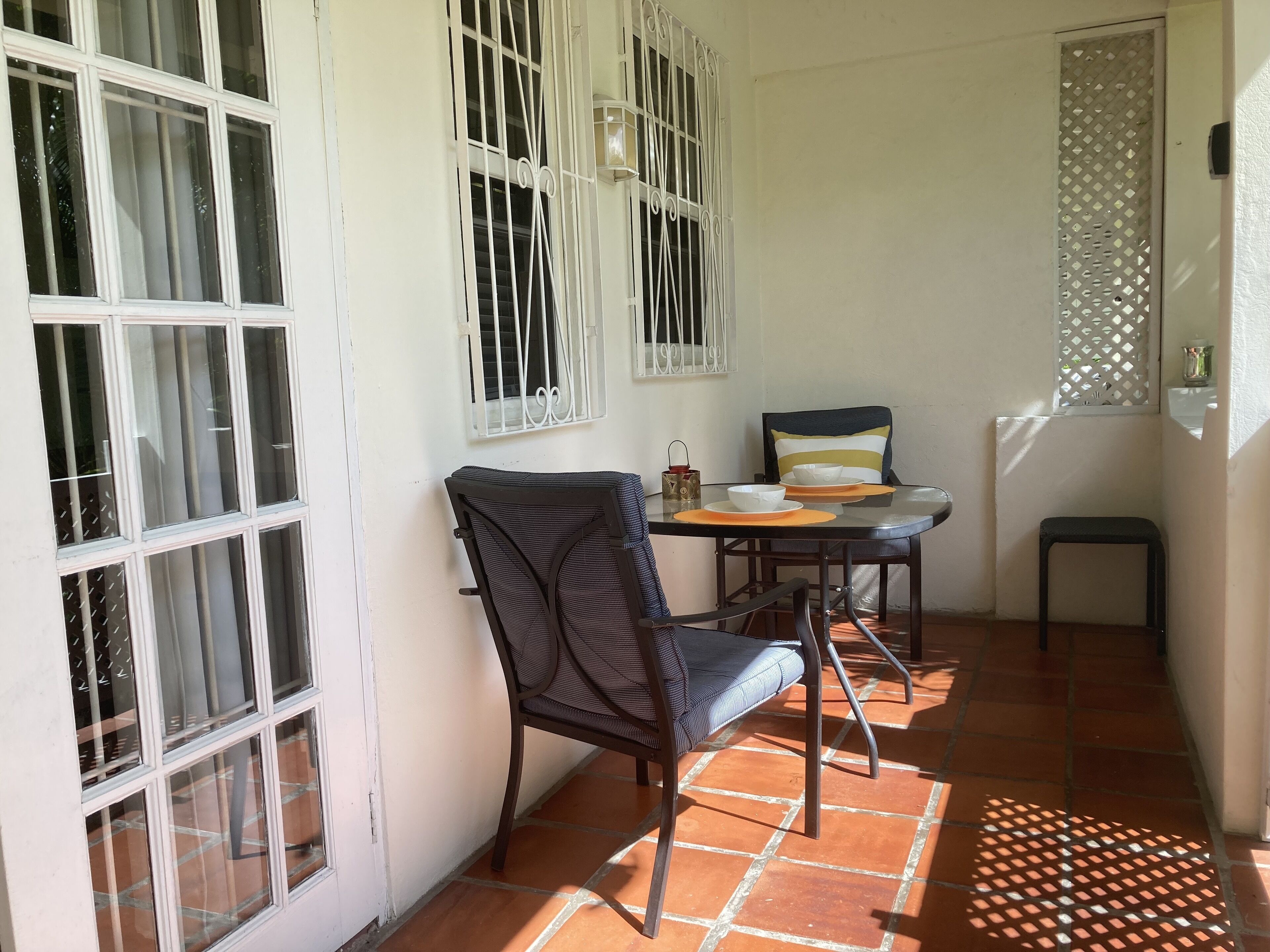 A small patio area with a table and chairs, a decorative lamp, and a window with metal bars.
