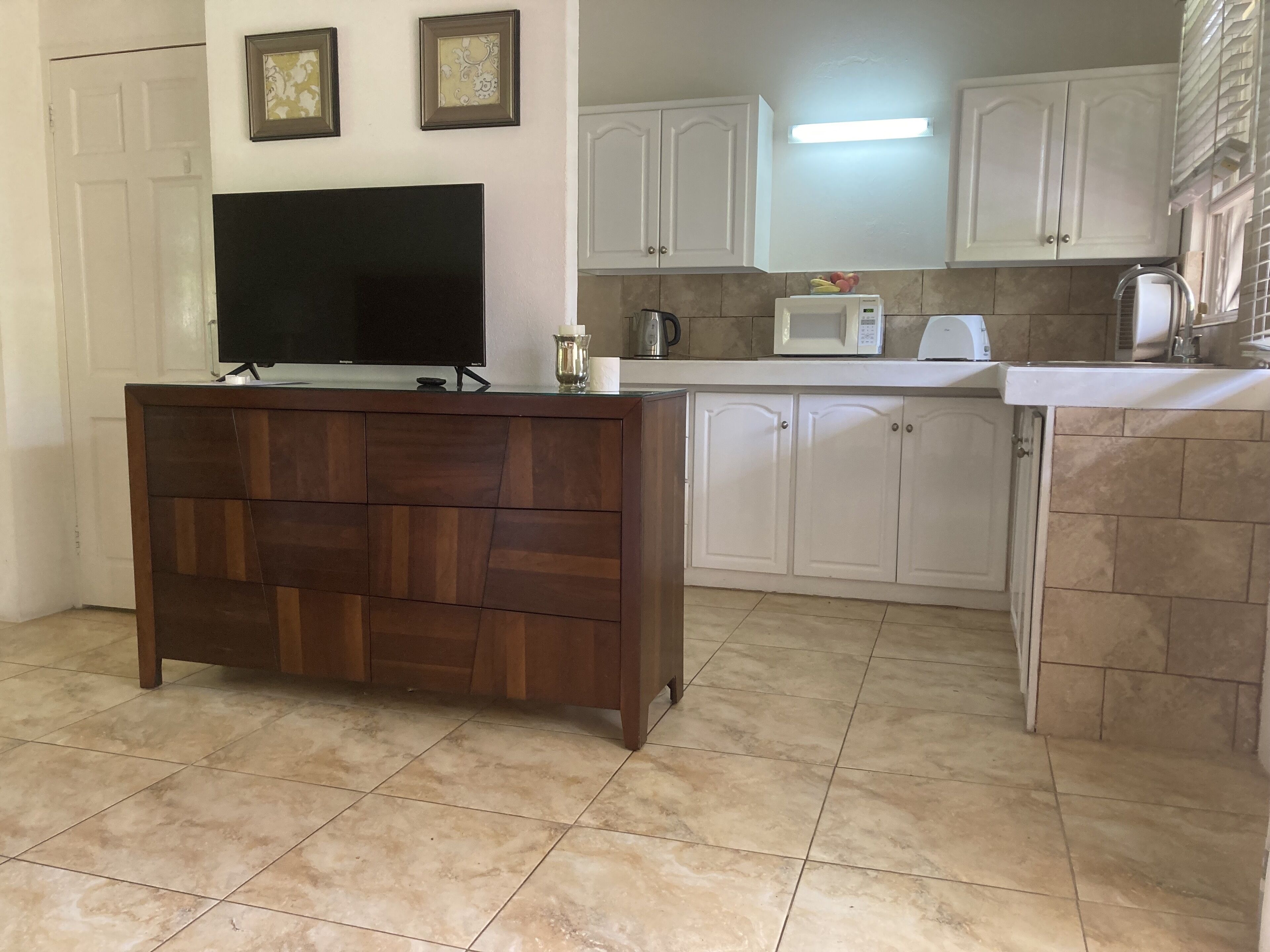 A kitchen with white cabinets, a wooden cabinet with a flat-screen TV, a microwave, and a kettle.