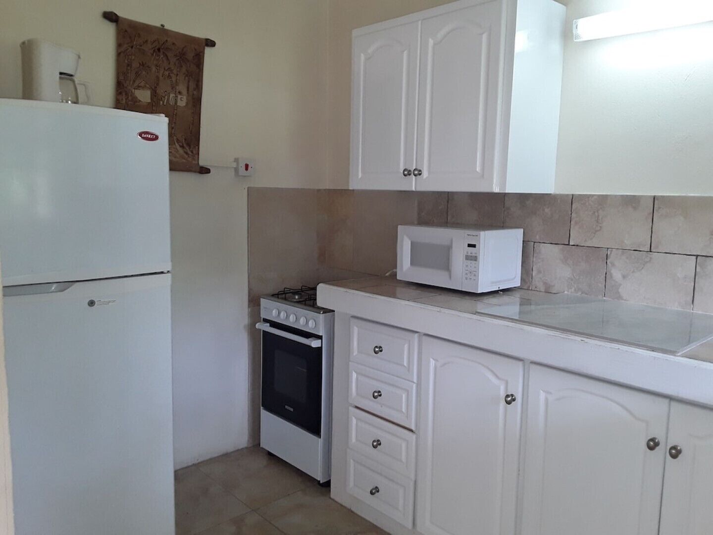 A compact kitchen with white cabinets, a refrigerator, a microwave, and a stove.
