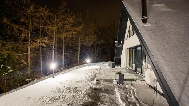 Un sendero cubierto de nieve que conduce a una casa moderna con techo inclinado y grandes ventanales.