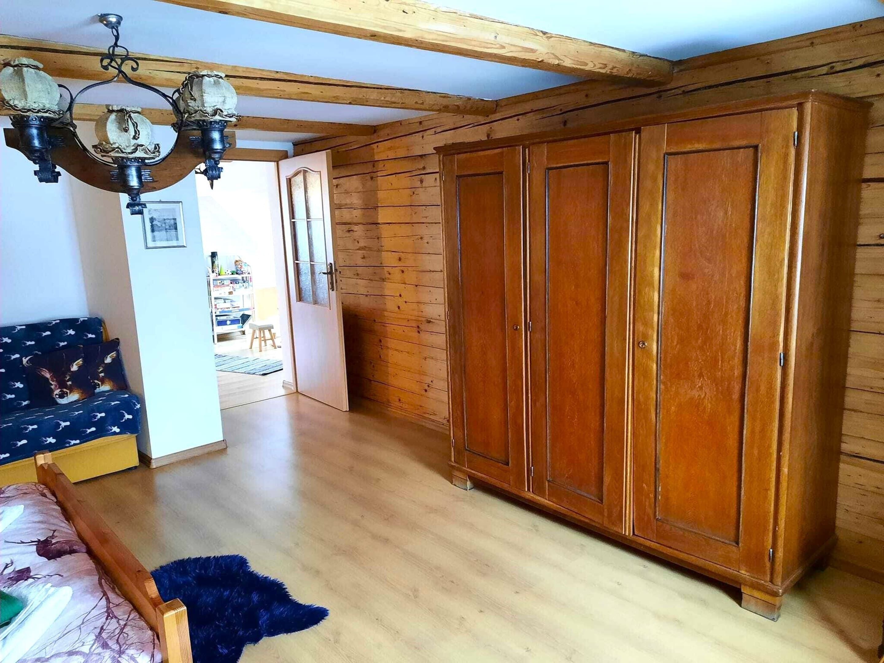 A room with wooden flooring, a wardrobe, a sofa, and a chandelier.