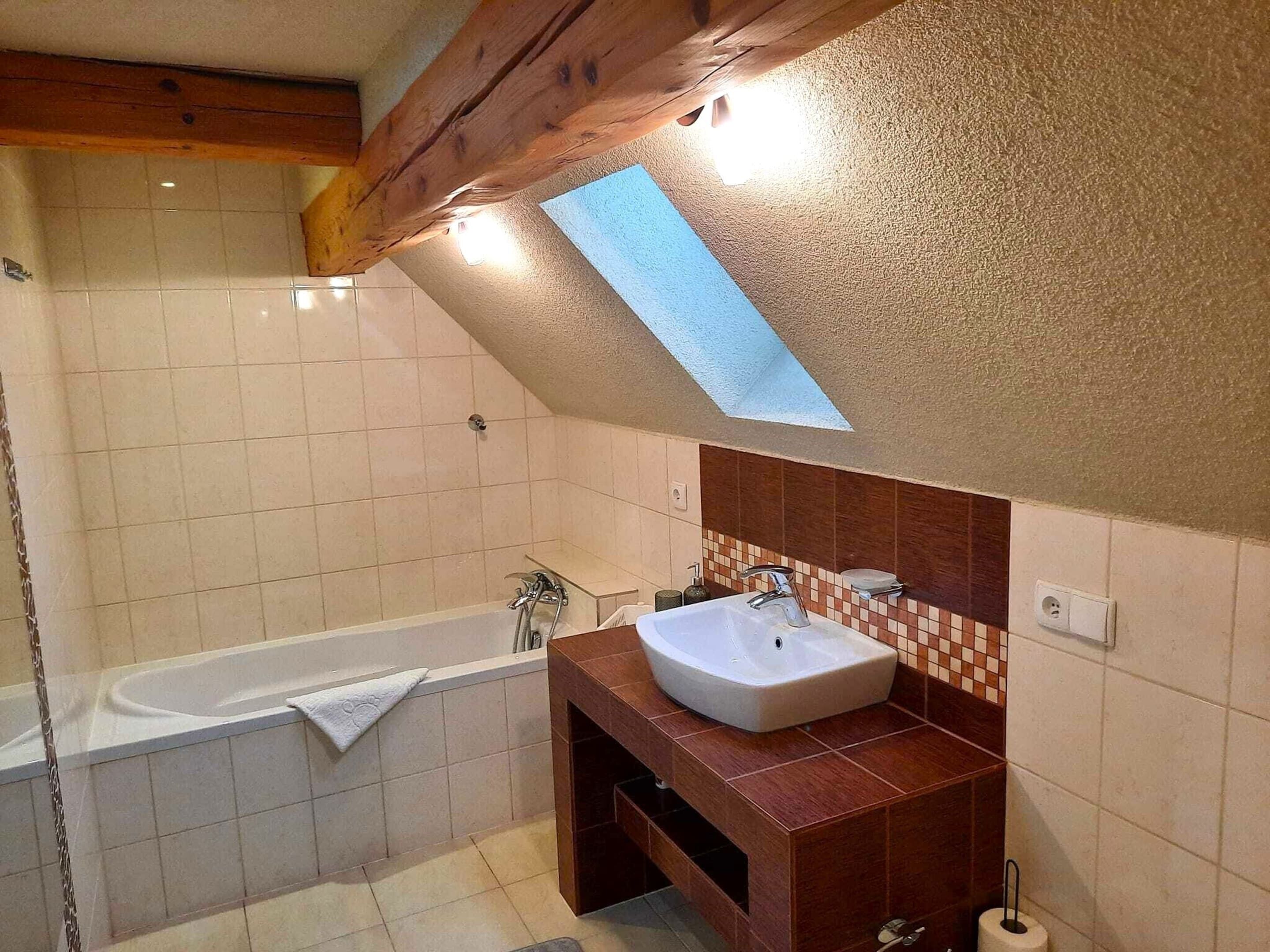 A modern bathroom with a freestanding bathtub, a wooden vanity with a sink, and a skylight above the vanity.
