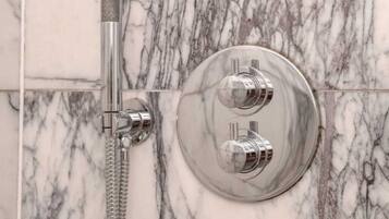 A bathroom with a marble shower wall, a handheld showerhead, and a wall-mounted control panel.