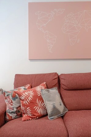 A red sofa with three decorative pillows against a wall with a geometric world map. - Bright 1 Bedroom Flat in Kensington Olympia (London)