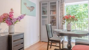 Ein Essbereich mit Tisch, Stühlen und einem Blumenstrauß. Ein Bücherregal und ein Fenster mit Blick ins Grüne.