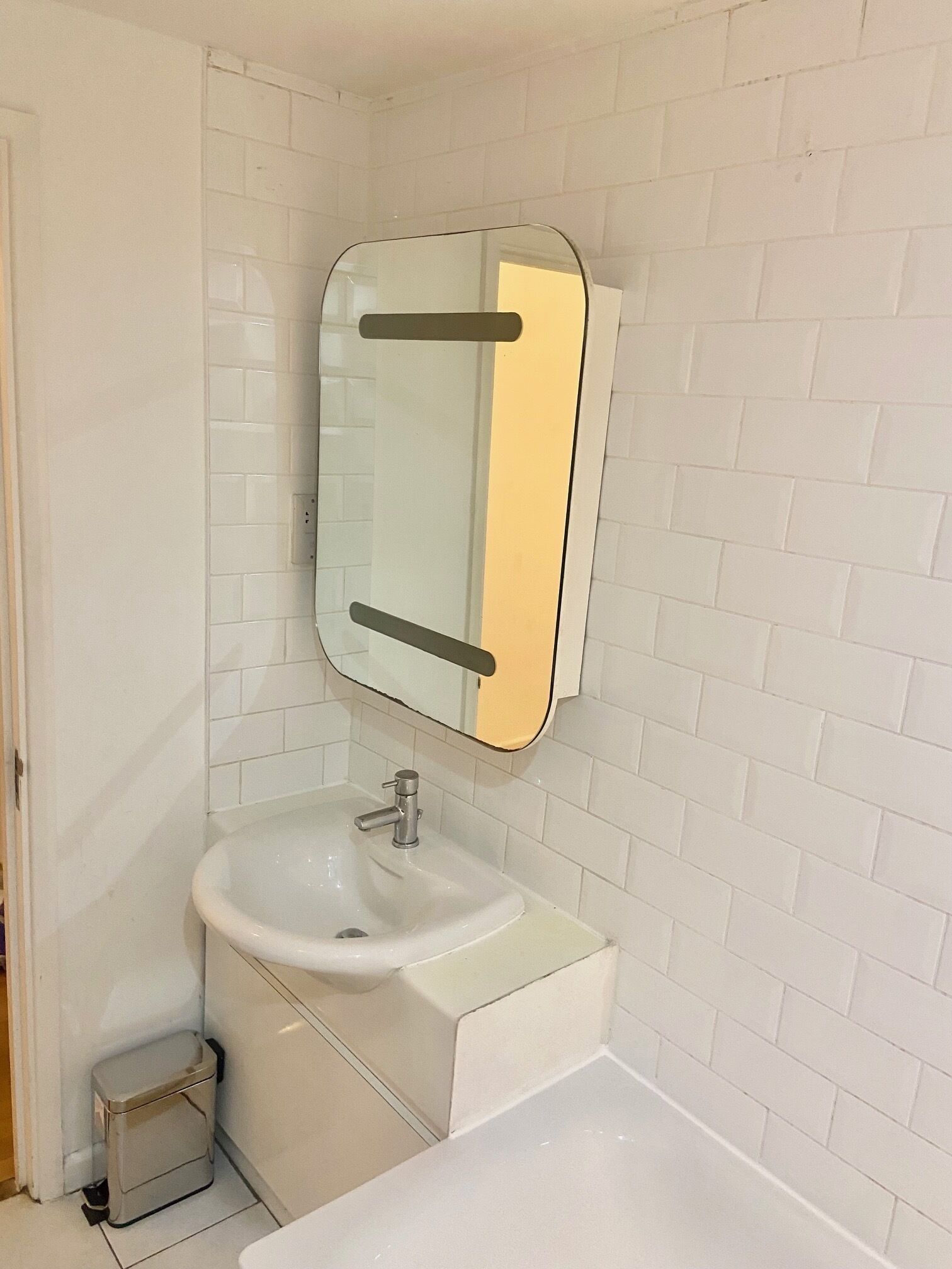 Un bagno con parete rivestita di piastrelle bianche, un lavandino bianco e uno specchio con cornice nera.