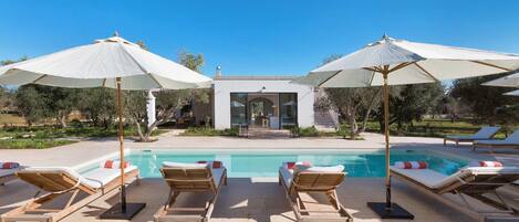 A pool area with lounge chairs and umbrellas, a clear sky, and a building in the background.