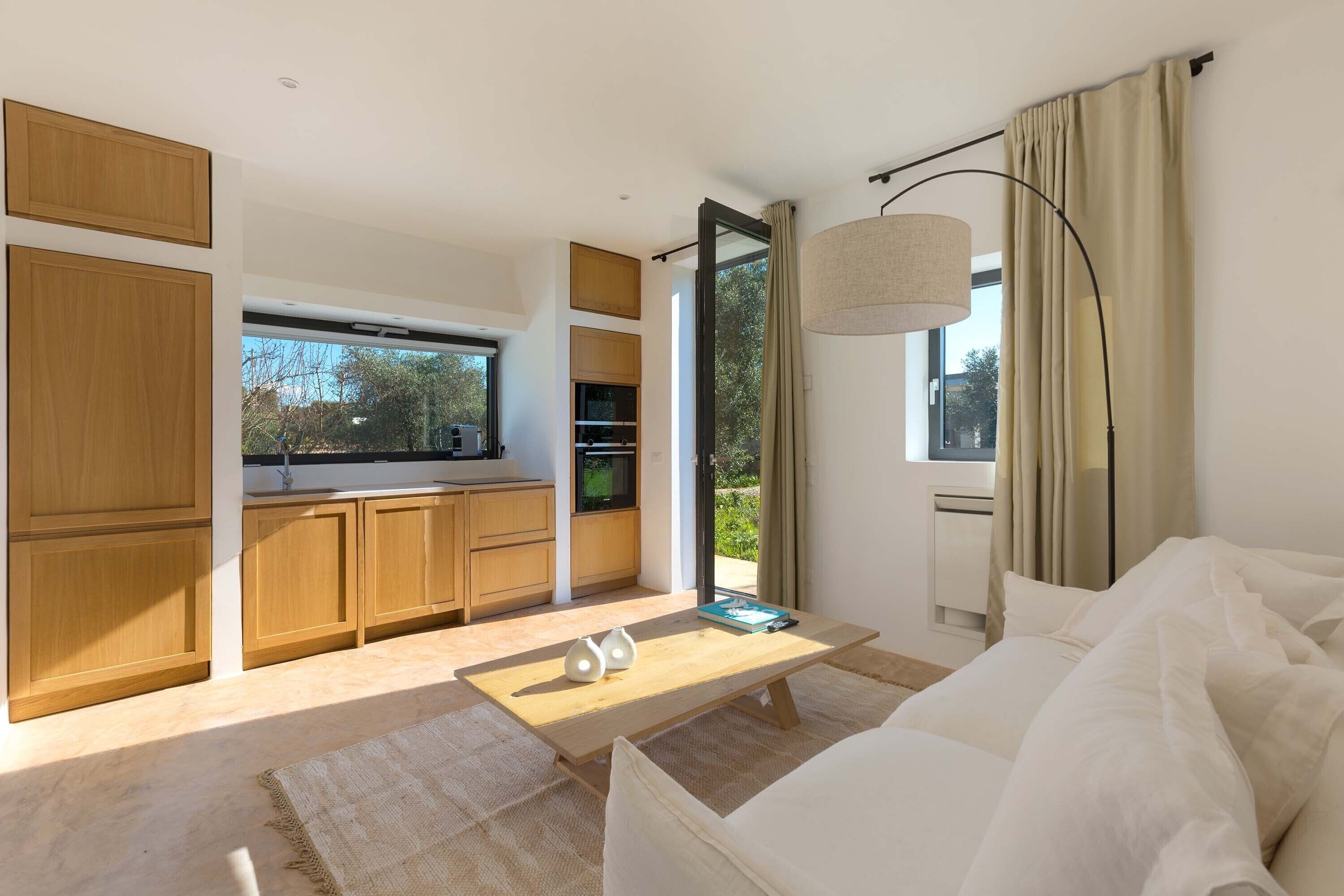 A modern living room with a sofa, a coffee table, and a view of a kitchen and outdoor area.