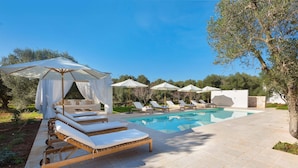 Un espace aménagé au bord de la piscine, avec des chaises longues, des parasols et un ciel d’un bleu limpide.