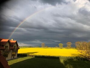 A rural landscape with a yellow field, a house with a red roof, and a rainbow in the sky. - Charming Holiday Home in Wolin With Terrace (gmina Wolin)