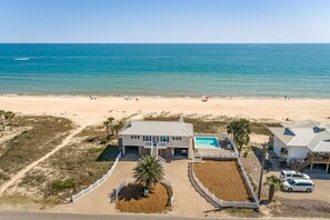 A beachfront property with a swimming pool, a fenced driveway, and a beach in the background.