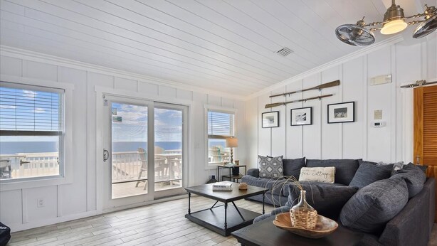A spacious living room with a large window, a dark-colored sofa, a coffee table, and a ceiling fan. - Welcome to One Fish Two Fish! (St. George Island)