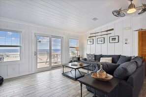 A spacious living room with a large window, a dark-colored sofa, a coffee table, and a ceiling fan.