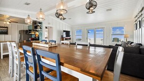 A spacious living area with a large wooden dining table, blue chairs, a dark gray sofa, and a view of the ocean through large windows. - Welcome to One Fish Two Fish! (St. George Island)
