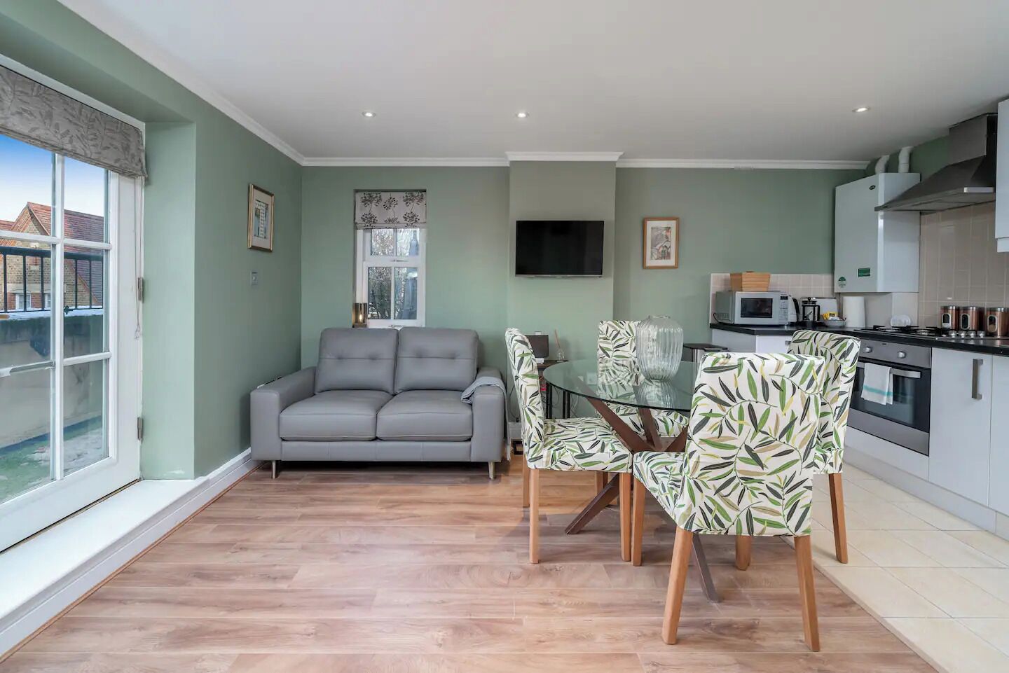 A living room with a grey sofa, a glass dining table, and patterned chairs.