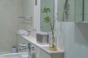 A modern bathroom with a glass shower enclosure, a white sink, and a vase with a plant on the countertop.