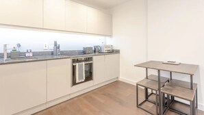 Una cocina moderna con armarios blancos, horno empotrado y una pequeña mesa de comedor con bancos.