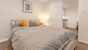 Un dormitorio con cama, mesita de noche, lámpara y un cuadro en la pared.