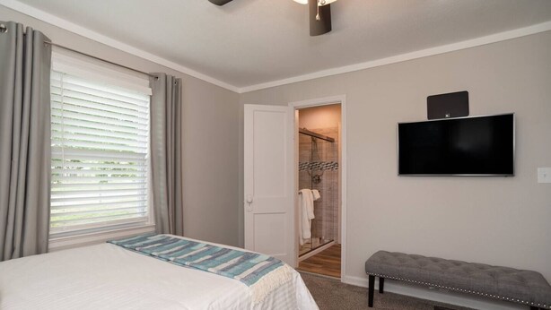 Un dormitorio con cama, un banco, televisor, ducha y puerta al baño.
