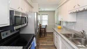 Una cocina moderna con armarios blancos, microondas integrado, pileta de acero inoxidable y un comedor con mesa y sillas.