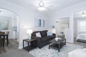A modern living room with a dark brown sofa, a coffee table, and a dining area with a wooden table and chairs.