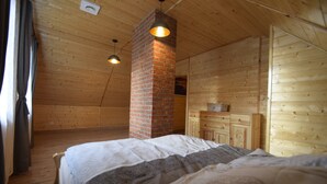 Un dormitorio acogedor con chimenea de ladrillo, paredes de madera y una cama con colcha estampada.