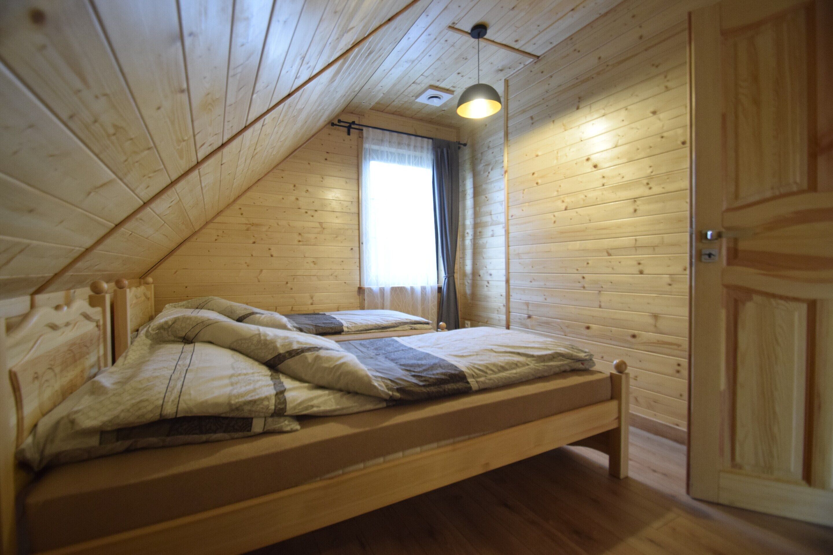 Un dormitorio de cabaña de madera con una cama individual, una ventana con cortinas y una puerta.