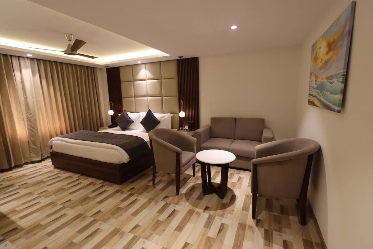 A modern hotel room with a bed, a sofa, a small table, and a painting on the wall.