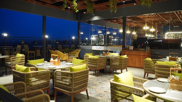 Un restaurant situé sur le toit, avec des meubles en osier, un espace bar et une vue sur la ville la nuit.