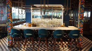 Un espace bar doté d’un comptoir blanc, de quatre tabourets de bar bleus et d’un sol à motifs.