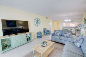 A living room with a TV, sofa, and coffee table. There is a starfish decoration on the cabinet and a sign that reads "Aloha Island". - 126 El Matador 2 Bedroom Condo by RedAwning (Fort Walton Beach)