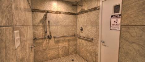 A small, tiled shower area with grab bars and a sign about sauna regulations.