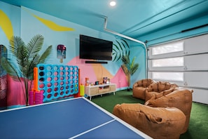 Una habitación con mesa de ping pong, sillones informales, televisor y un llamativo mural de colores.