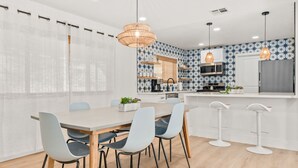 A modern kitchen with white cabinets, a central island, and a dining area with a wooden table and chairs. - New Listing! Desert Oasis ~ Hot Tub (Twentynine Palms)
