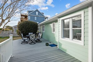 Een terras met tuinmeubilair, een kleine tuin en een huis met lichtgroene bekleding en witte details.