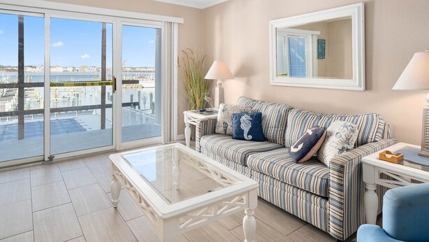 A living room with a striped sofa, a glass coffee table, and a view of the city through large sliding doors.