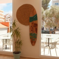 Una habitación con un ventanal amplio, una planta en maceta y una tabla de surf colgada en la pared.
